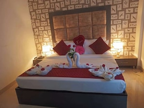 A hotel room with a neatly made bed, a headboard with a decorative panel, two bedside tables with lamps, and a wall with framed pictures. - Hotel Royal Regency (Dera Bassi)