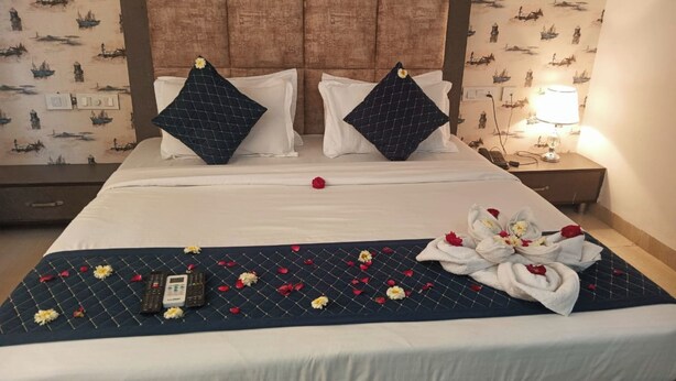 Un letto rifatto con una coperta blu, cuscini bianchi e un vaso di fiori sul comodino.