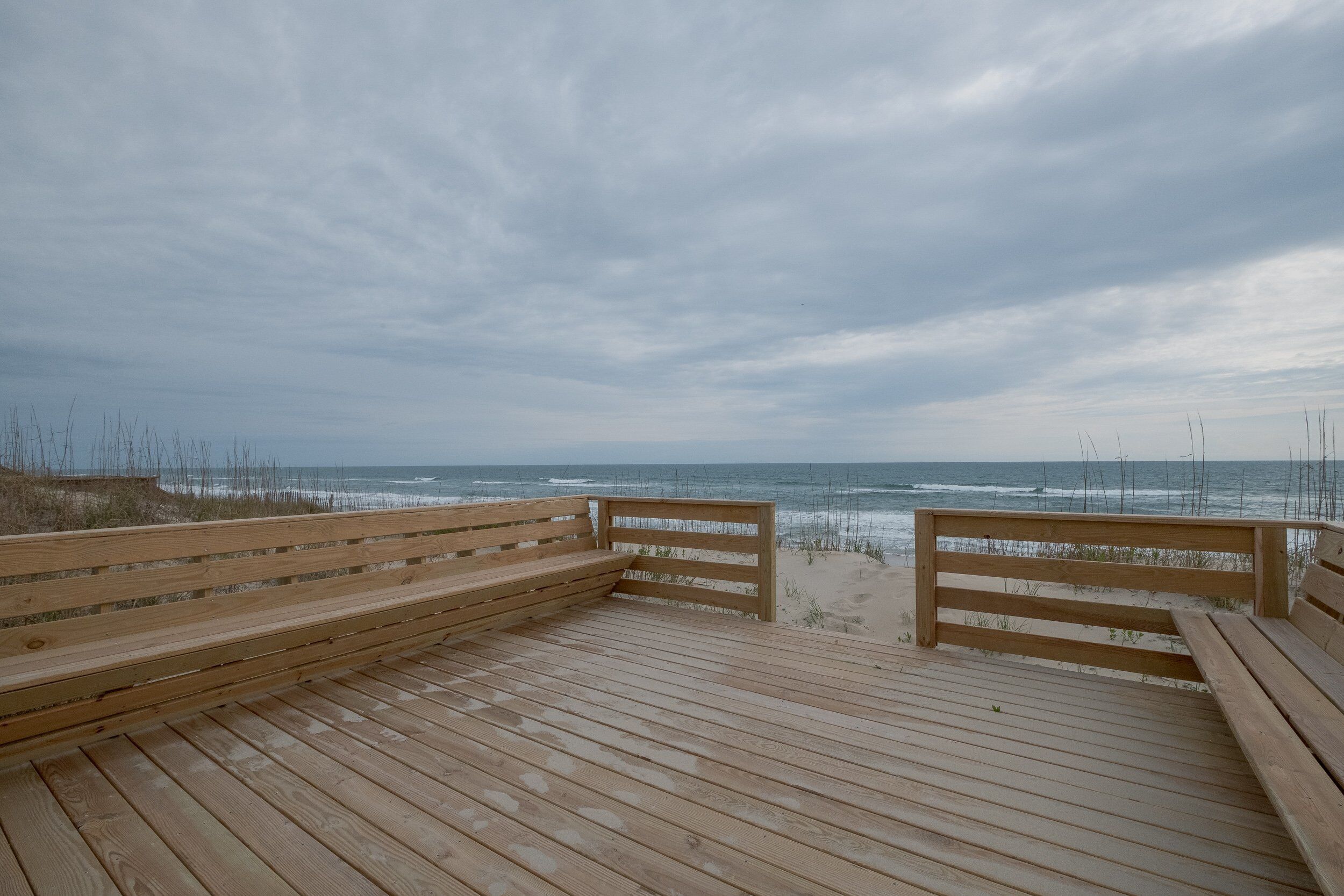 Een houten terras met banken, met uitzicht op een strand en zee.