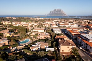 A residential area with houses, a swimming pool, and a mountain in the background. - Casa Carlotta by Wonderful Italy (Loiri Porto San Paolo)