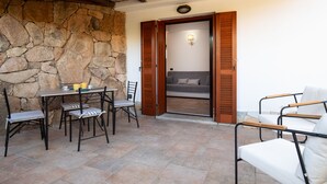 A stone wall, a wooden door, a sofa, and a table with chairs. - Casa Carlotta by Wonderful Italy (Loiri Porto San Paolo)