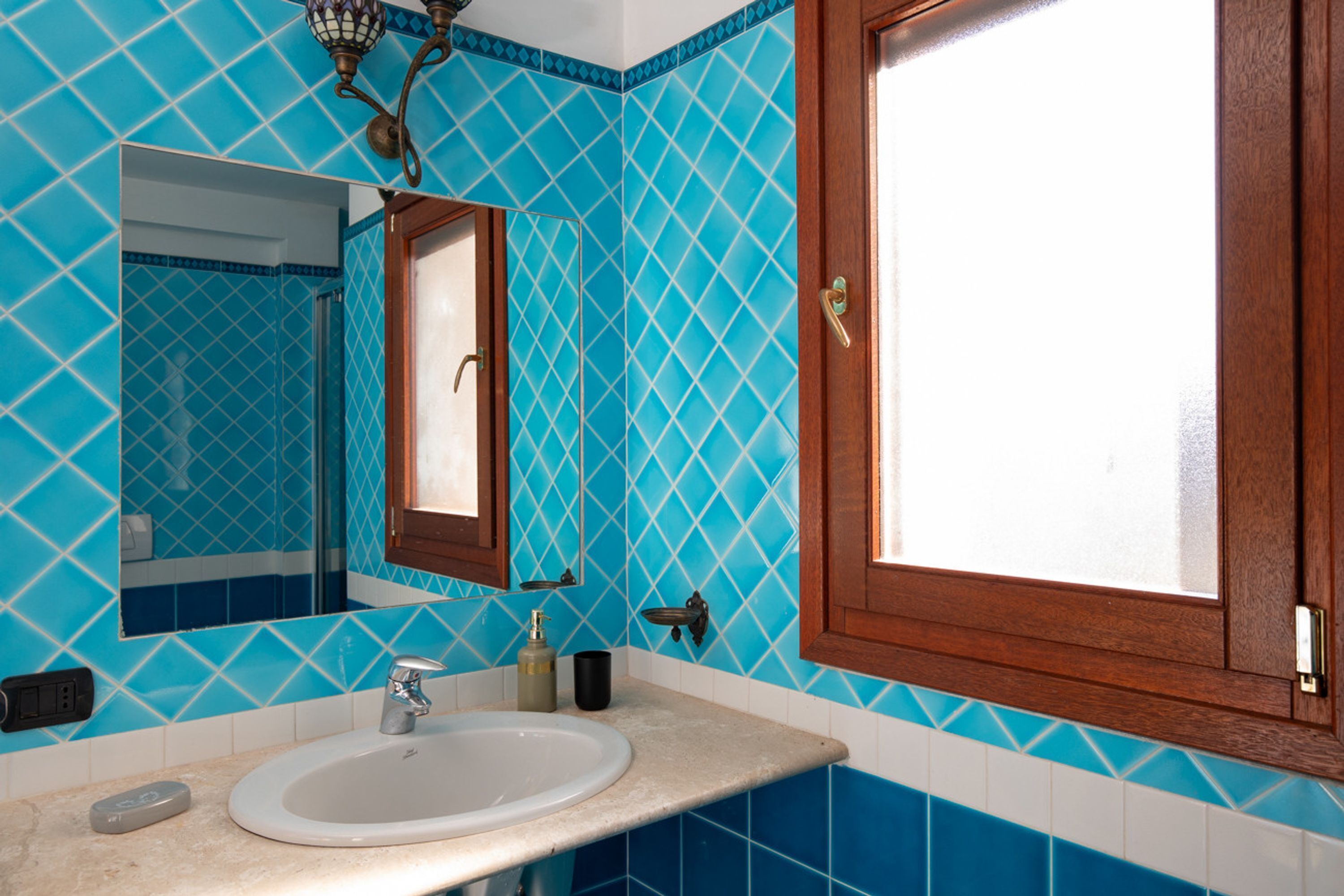 Casa de banho com pia, espelho e paredes revestidas de azulejos azuis.