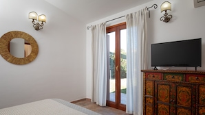 A bedroom with a bed, a television on a cabinet, a mirror, and curtains on a sliding door. - Casa Carlotta by Wonderful Italy (Loiri Porto San Paolo)