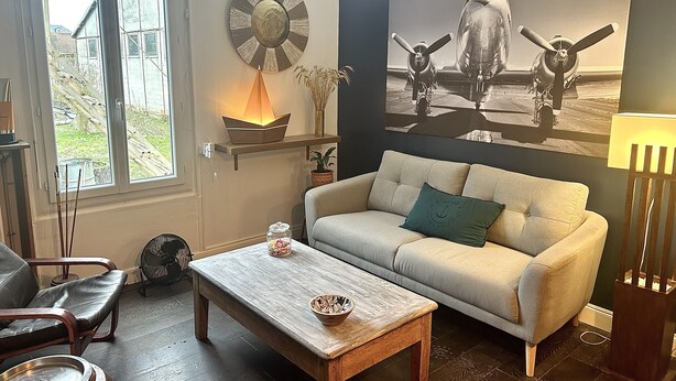 A living room with a sofa, a coffee table, a lamp, a wall clock, and a large airplane painting. - Maison de Ville Avec Jardin Proche du Pont Canal (Briare)