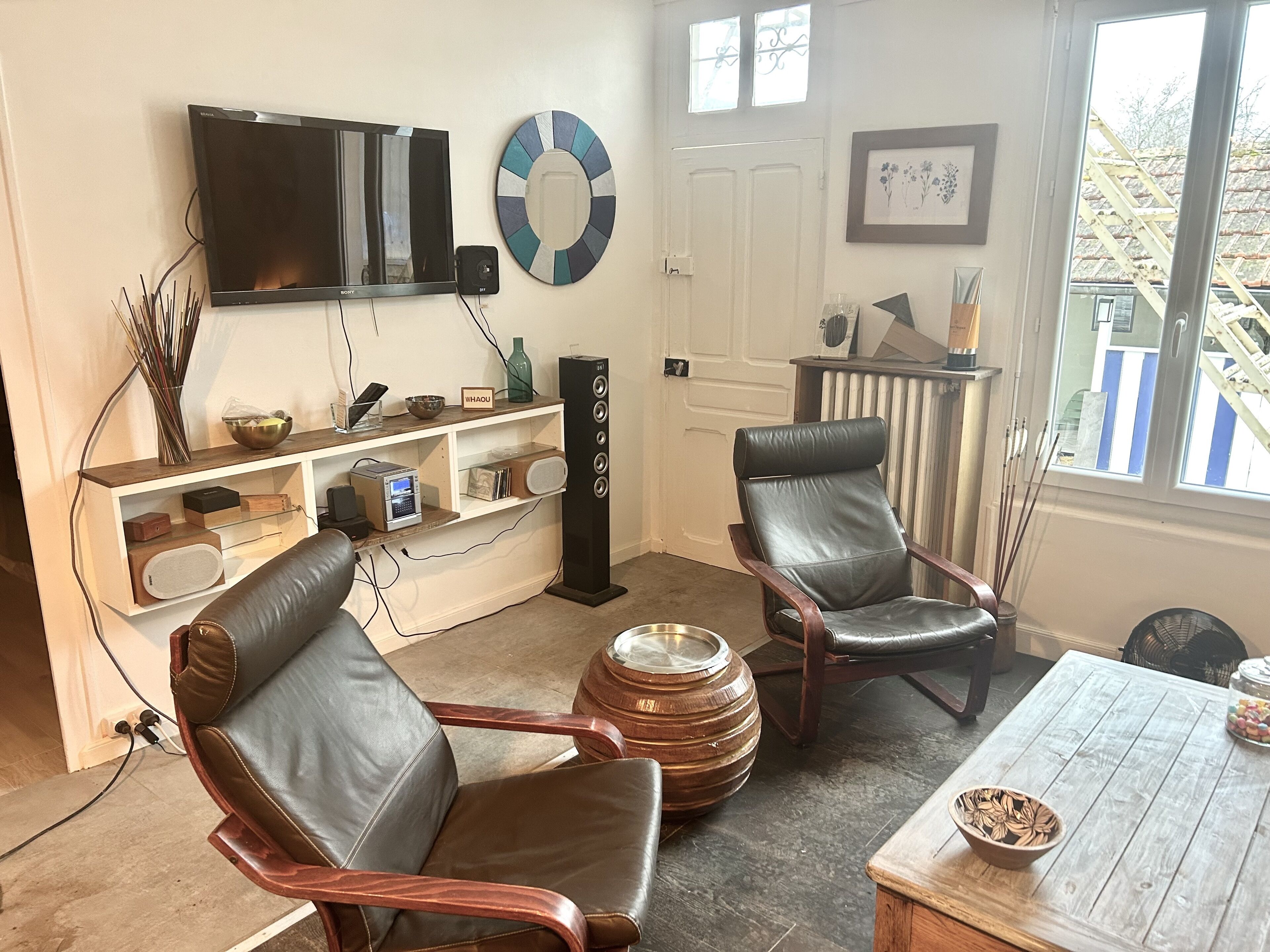 A living room with a television, a decorative wall clock, a fireplace, and a view of the outside.