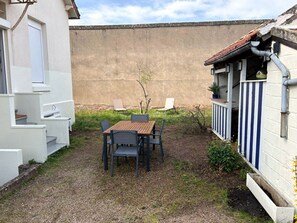 A patio with a table and chairs, a small garden, and a building with a striped exterior. - Maison de Ville Avec Jardin Proche du Pont Canal (Briare)