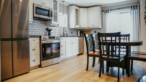 Une cuisine moderne dotée d’appareils électroménagers en acier inoxydable, de meubles blancs et d’une table à manger en bois avec des chaises.