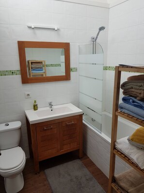 A bathroom with a white sink, wooden vanity, a glass shower enclosure, and a towel rack with folded towels.