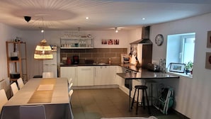 A modern kitchen with white cabinets, a dining table with chairs, a hanging light fixture, and a window with a view. - House, Central Village location, near cafe/boulangerie, 300m from coast. (Saint Armel)