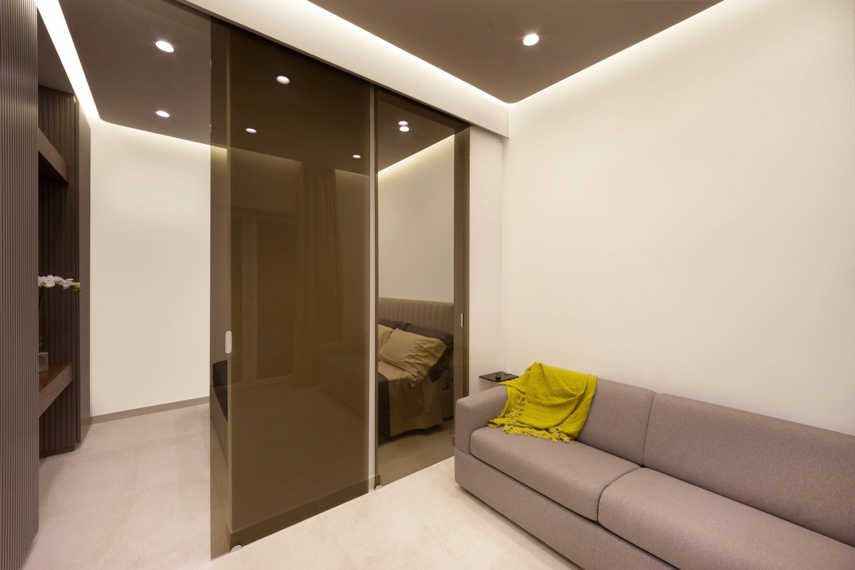 A modern bedroom with a sliding glass door closet, a grey sofa, and a yellow throw blanket.