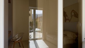 Une chambre moderne dotée d’une porte-fenêtre coulissante donnant sur un balcon, d’une chaise en verre et d’un lit avec une tête de lit.