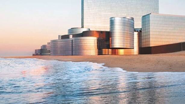 Ein modernes Gebäude mit einer großen Glasfassade, gelegen an einem Strand mit ruhiger See im Vordergrund.