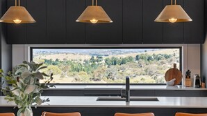 A modern kitchen with a large window overlooking a scenic landscape, a sink, and three pendant lights. - 1B Alpine View Retreat - 4BR Luxurious Escape l Mountain Views l Fast WiFi (Jindabyne)