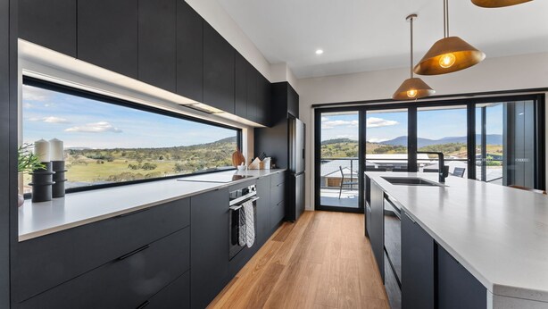 A modern kitchen with dark cabinetry, a large window, and a view of the countryside. - 1B Alpine View Retreat - 4BR Luxurious Escape l Mountain Views l Fast WiFi (Jindabyne)