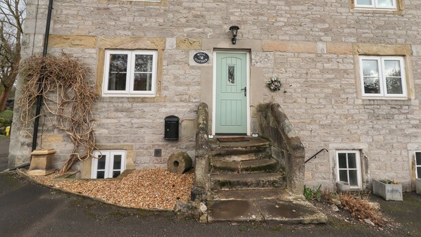 Une petite maison en pierre avec une porte verte, un petit porche et un chemin de gravier menant à l’entrée.
