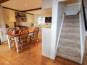 Una cocina con suelo de madera, armarios blancos y una zona de comedor con una mesa y sillas de madera.