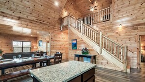 A log cabin interior with a dining area, kitchen, and a staircase leading to an upper level. - New! Pet Friendly, Private Pool, Media Room, Golf! (Sevierville)
