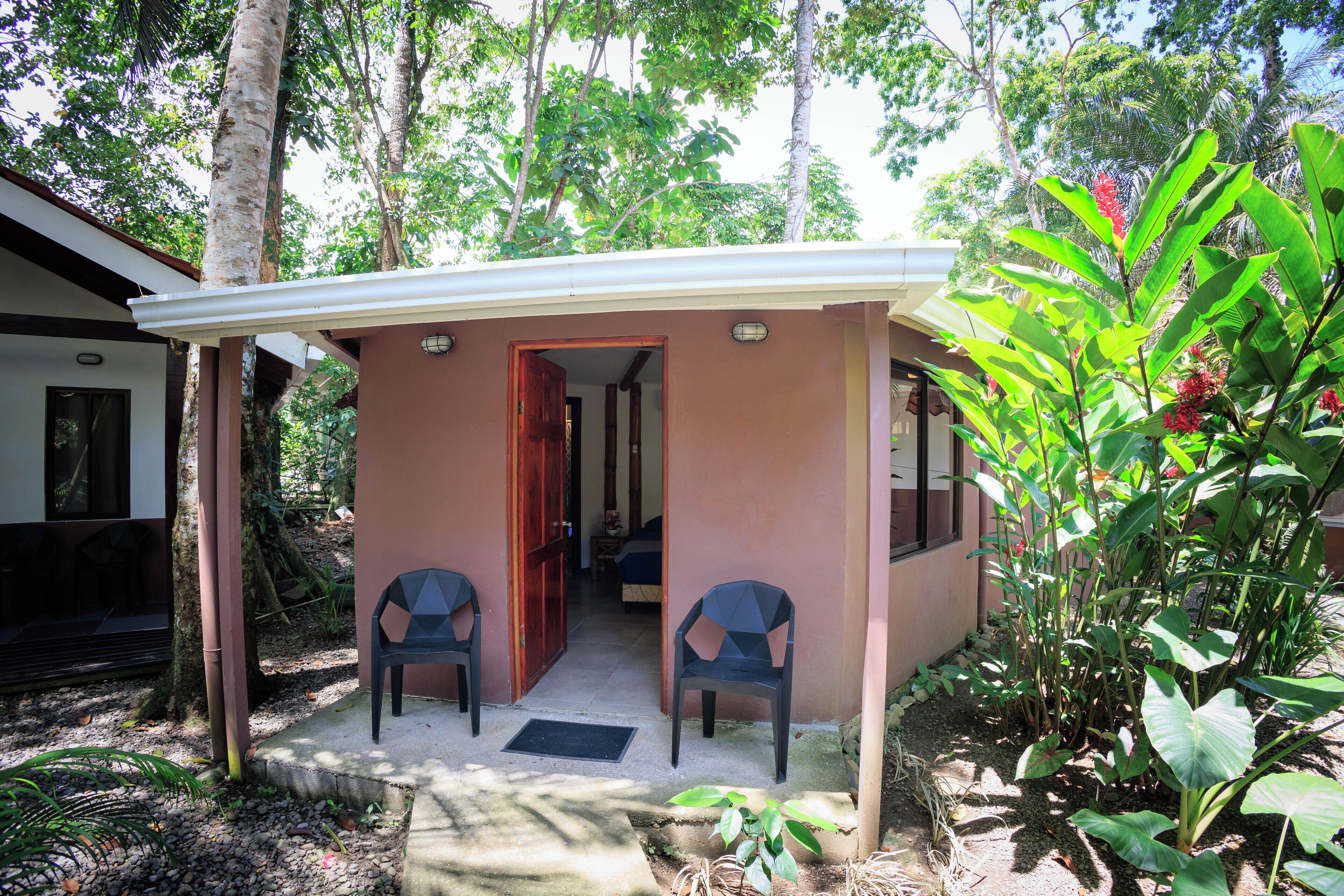 A small, single-story building with a covered porch, two chairs, and a door leading inside.