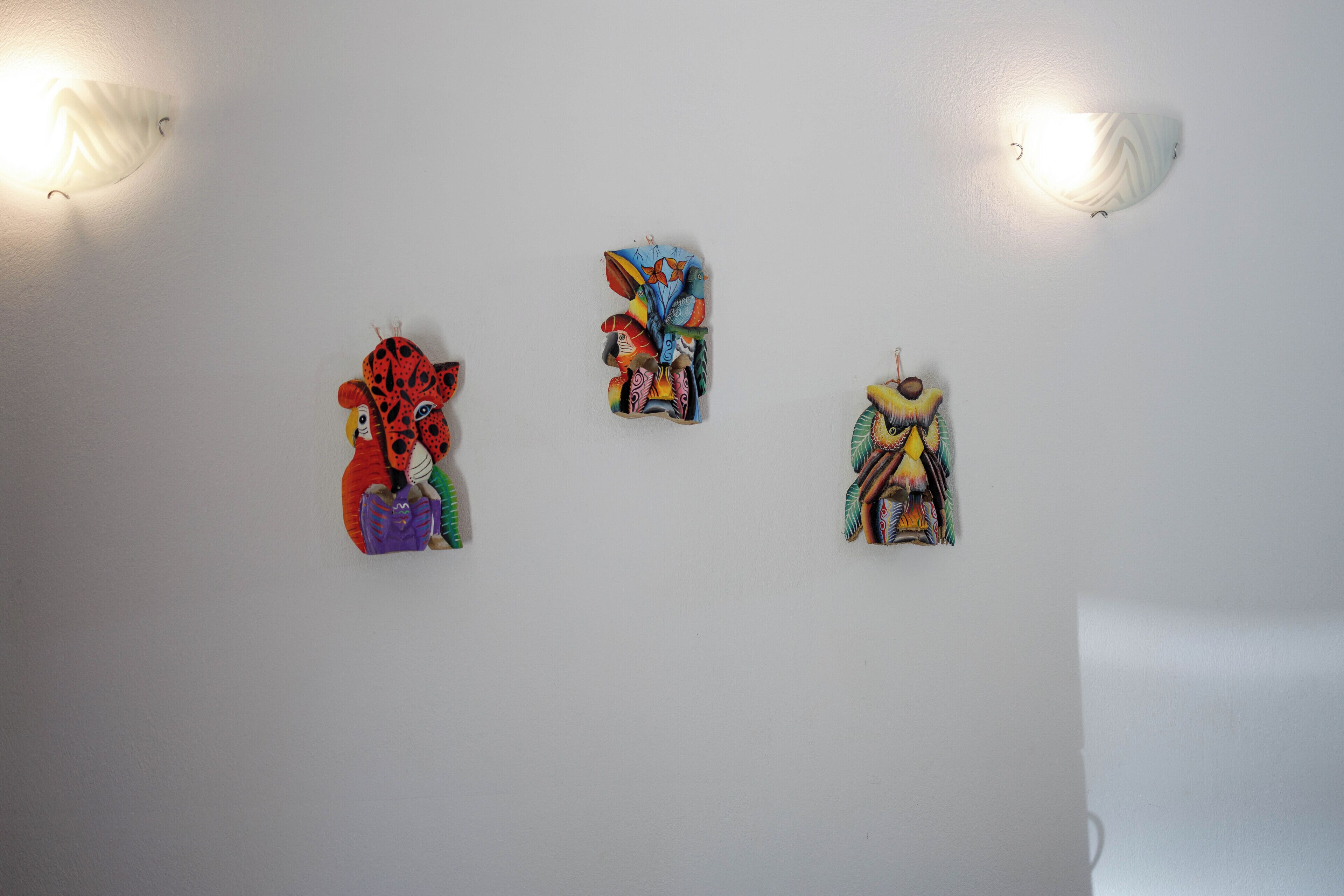 Three wall-mounted artworks in a room with white walls and two wall-mounted lights.