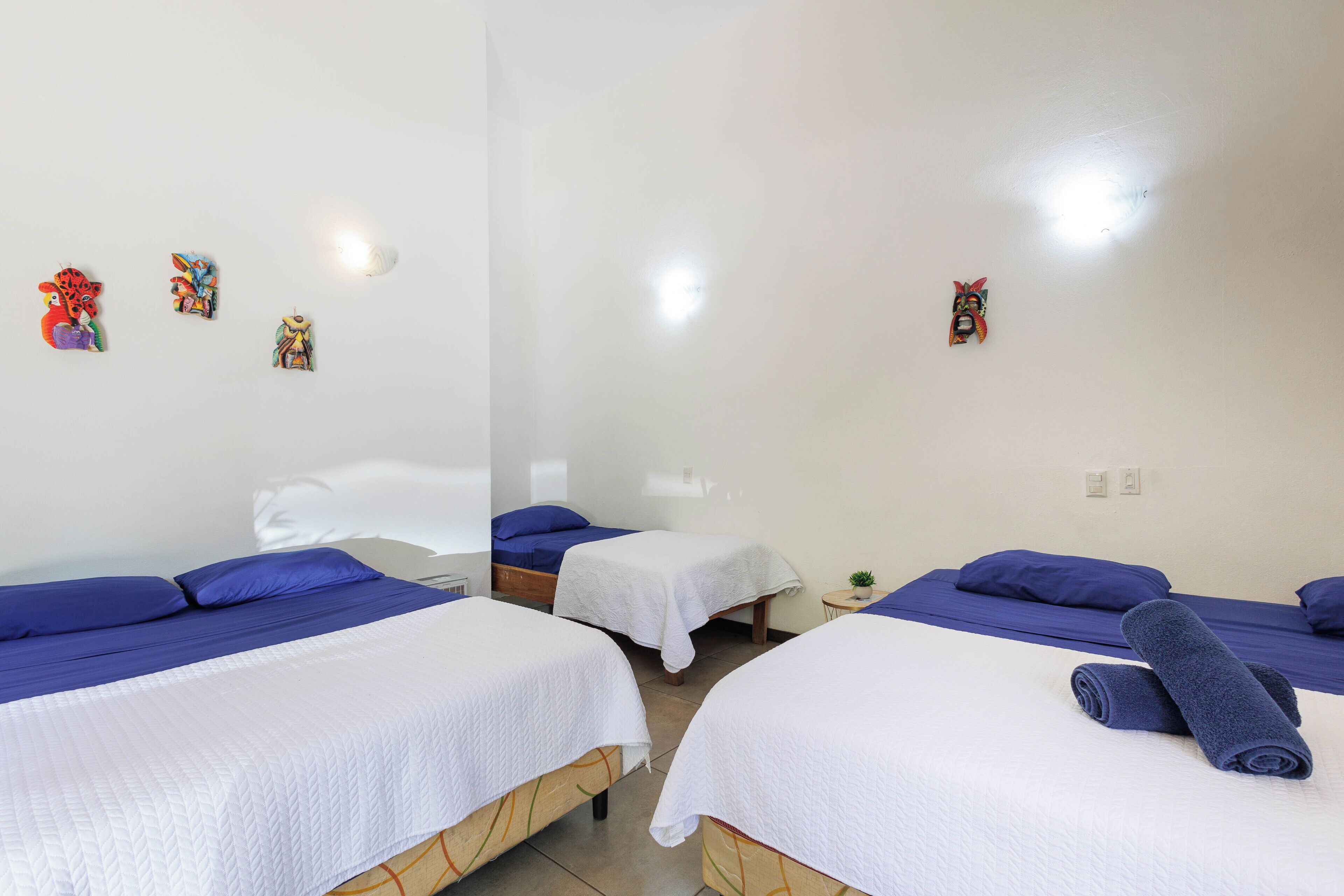 Une chambre d’hôtel avec deux lits, du linge de lit blanc et des oreillers bleus. Les murs sont décorés et il y a une petite plante sur la table de chevet.