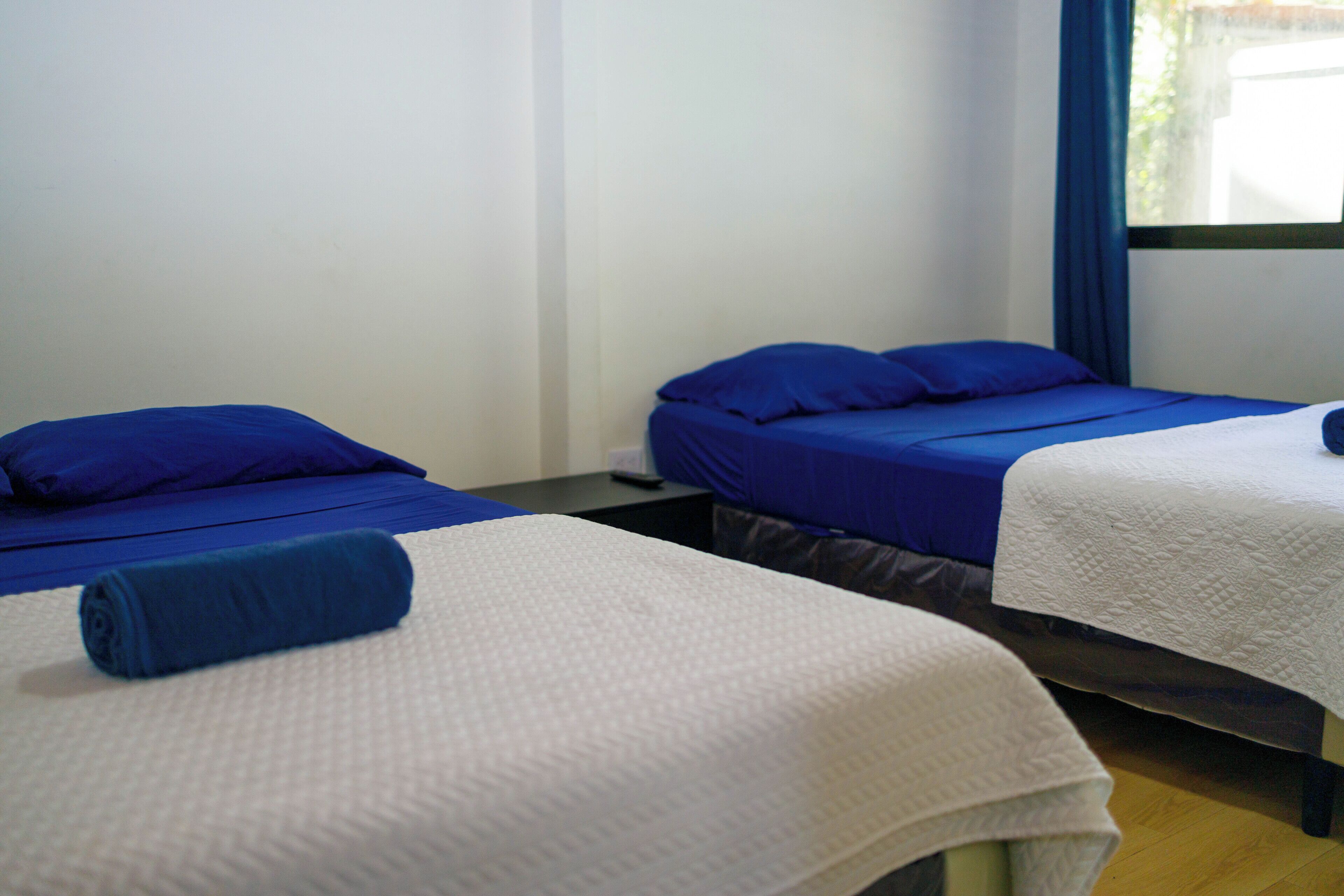 Een hotelkamer met twee bedden, één met blauw beddengoed en de ander met wit beddengoed.