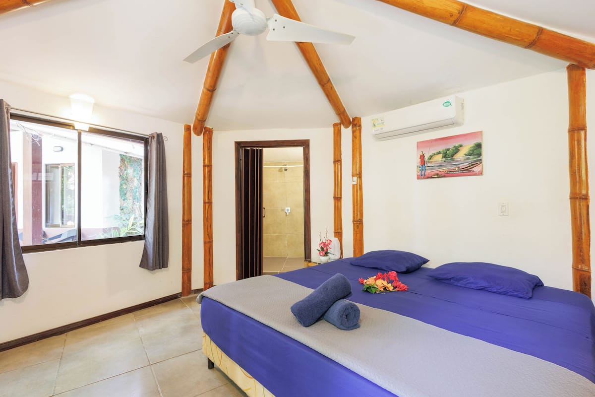 A bedroom with a bed, a ceiling fan, a window with curtains, and a painting on the wall.