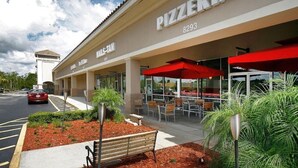 Eine Pizzeria mit Außenbereich, einem roten Markisen und einem Parkplatz im Hintergrund.