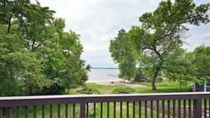 A deck with a view of a lake, surrounded by trees and a grassy area. - Sandy Shore Lodge- beautiful, private sand beach awaits! (Shell Lake)
