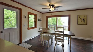 A dining area with a table and chairs, a ceiling fan, and windows with views of greenery. - Sandy Shore Lodge- beautiful, private sand beach awaits! (Shell Lake)