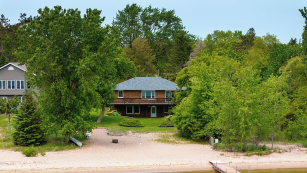 A two-story house with a balcony, surrounded by trees and a sandy beach. - Sandy Shore Lodge- beautiful, private sand beach awaits! (Shell Lake)