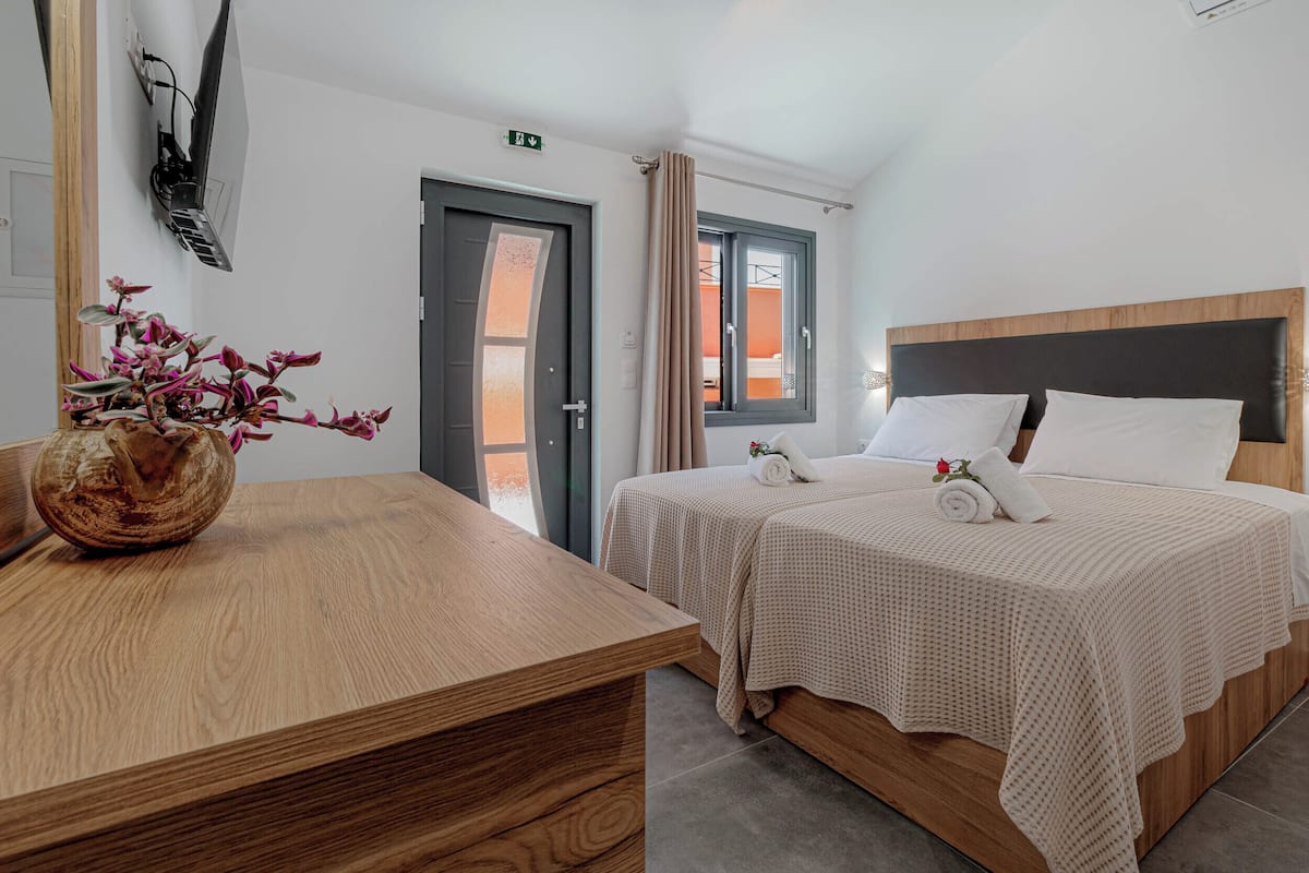 A hotel room with a wooden bed, a wooden desk, a vase with flowers, and a window with curtains.