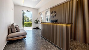 A modern reception area with a wooden reception desk, a sofa with cushions, and a large clock on the wall. - Ionian Arches Corfu (Corfu)