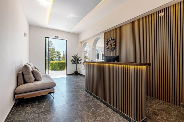 Una moderna zona de recepción con un mostrador de madera, un sofá con cojines y un reloj grande en la pared.