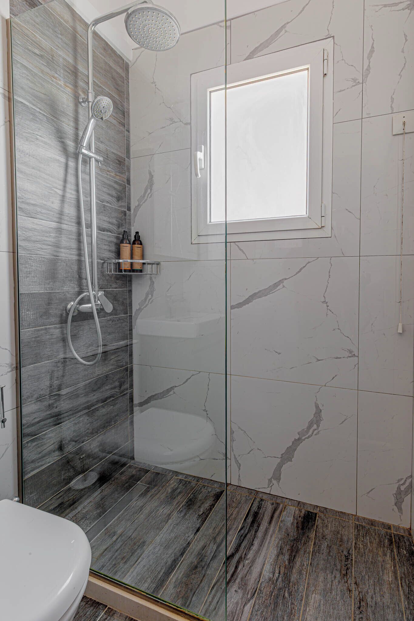 A modern bathroom with a glass-enclosed shower, a toilet, and a shelf with toiletries.