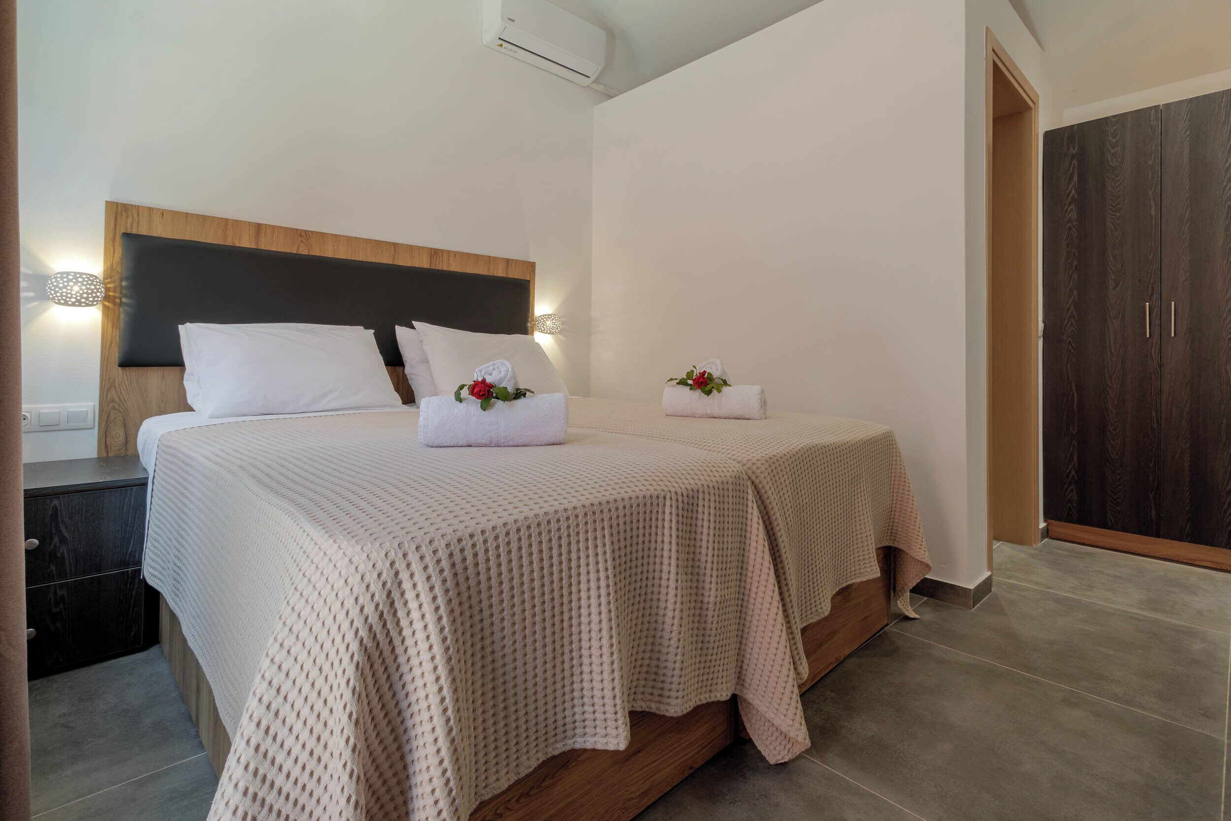 A double bed with a textured beige bedspread, a wooden headboard, and two bedside tables with lamps.
