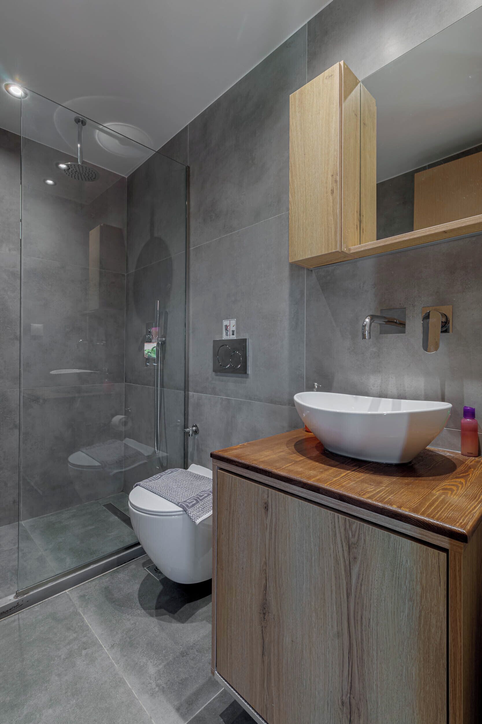 A modern bathroom with a glass-enclosed shower, a white sink with a wooden countertop, and a wooden cabinet.