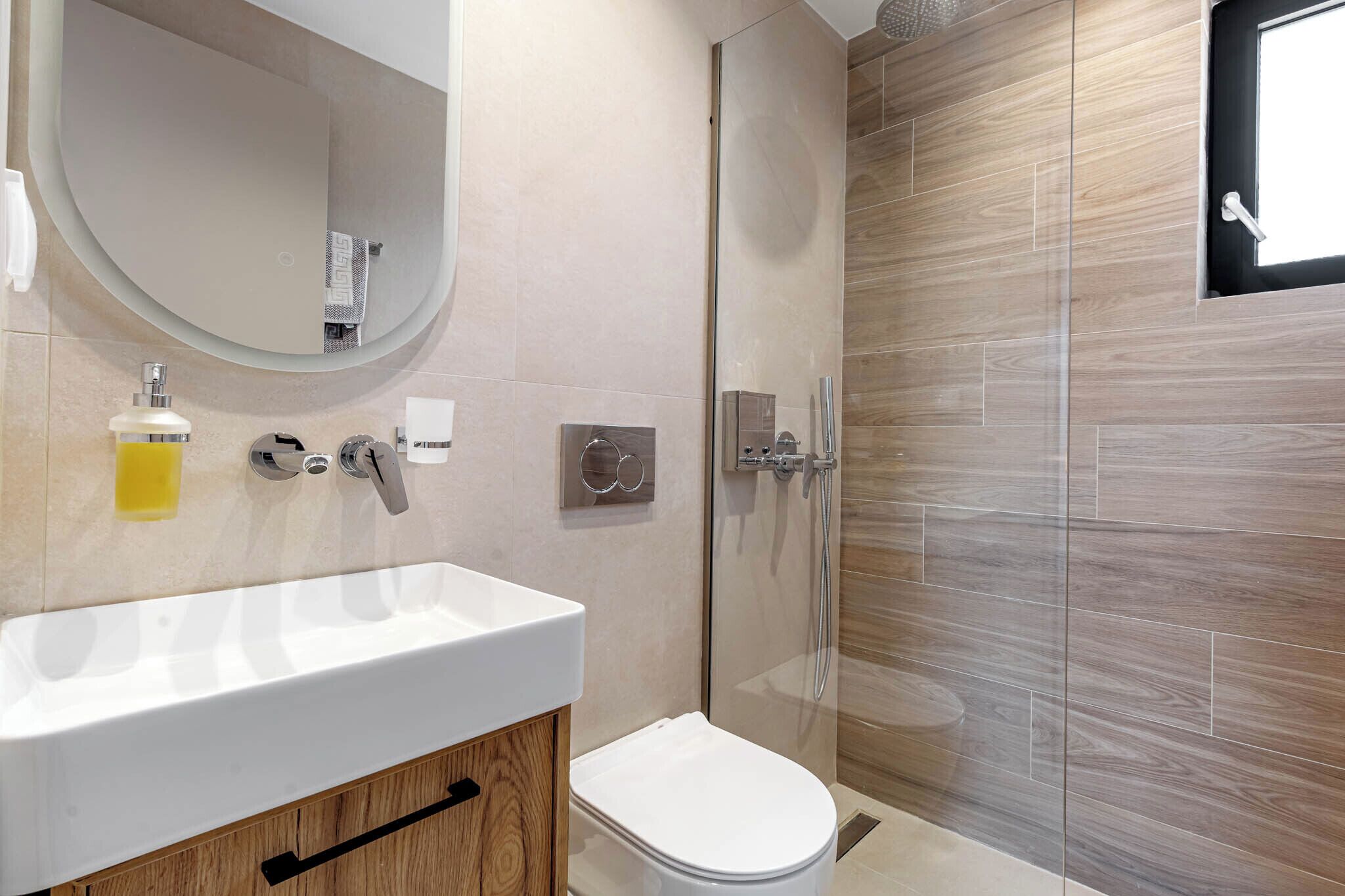 Un baño moderno con un lavamanos blanco, un inodoro y una ducha con mampara de vidrio.