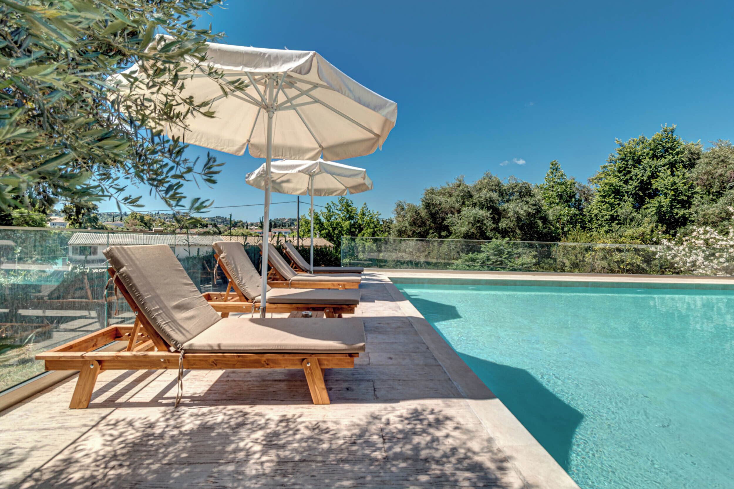 Un espace aménagé au bord de la piscine, avec des chaises longues en bois et des parasols de couleur beige.