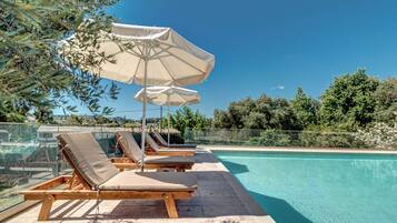 Un espace aménagé au bord de la piscine, avec des chaises longues en bois et des parasols de couleur beige.