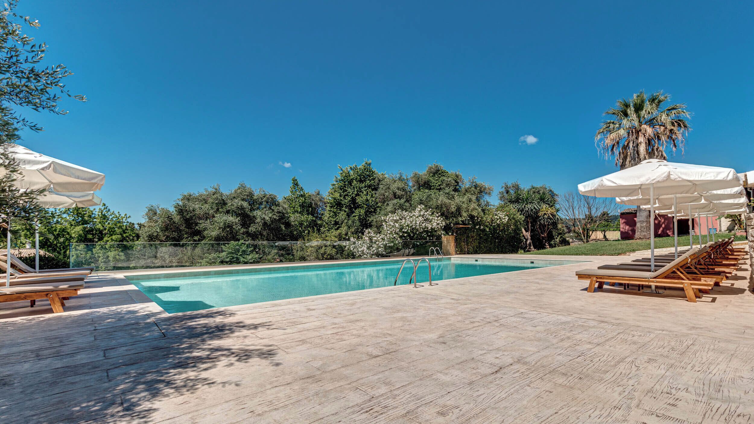 A rectangular swimming pool with a wooden deck, lounge chairs, and umbrellas.