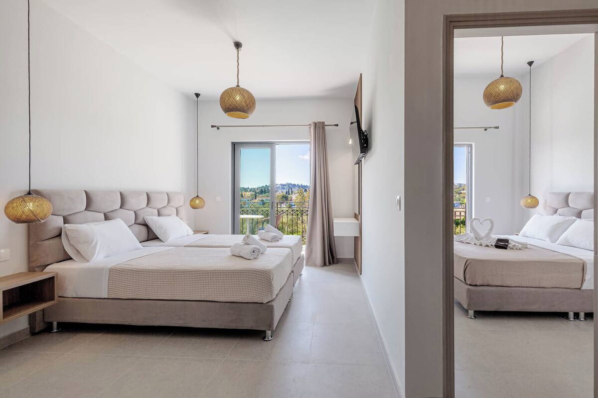 A modern bedroom with a large bed, bedside tables, a TV, and a balcony with a view.