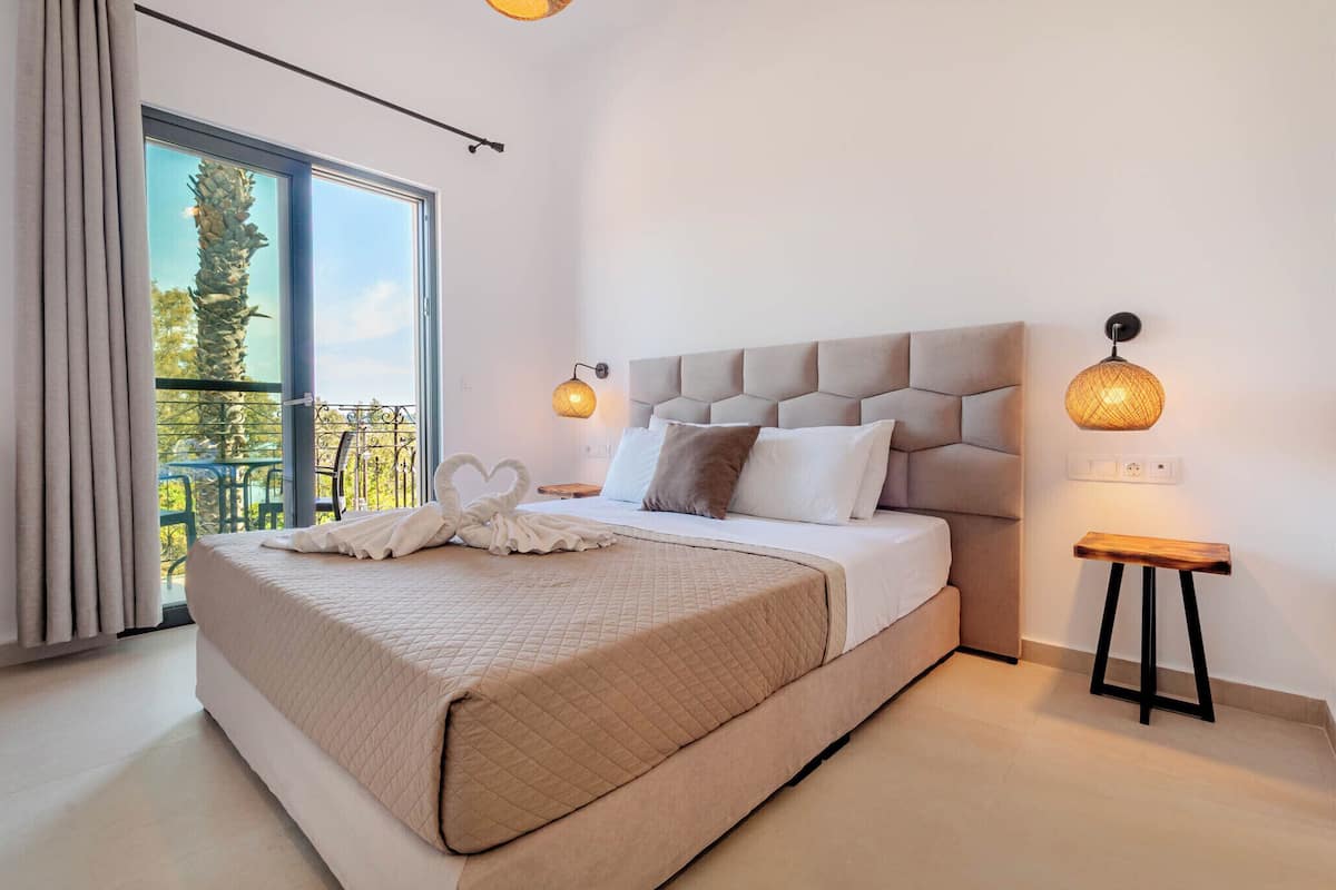 A modern bedroom with a large bed, a balcony view, and two wall-mounted lamps.