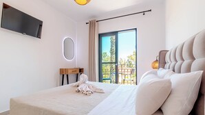 A modern hotel room with a large bed, a flat-screen TV mounted on the wall, a wooden nightstand, and a balcony with a view of trees and a railing. - Ionian Arches Corfu (Corfu)