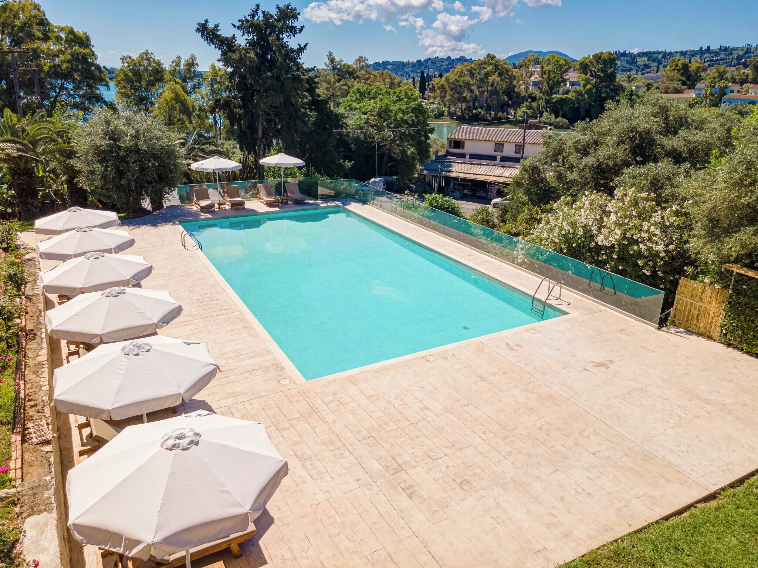 A rectangular swimming pool with a clear blue water, surrounded by a wooden deck. There are several white umbrellas and lounge chairs along the poolside.
