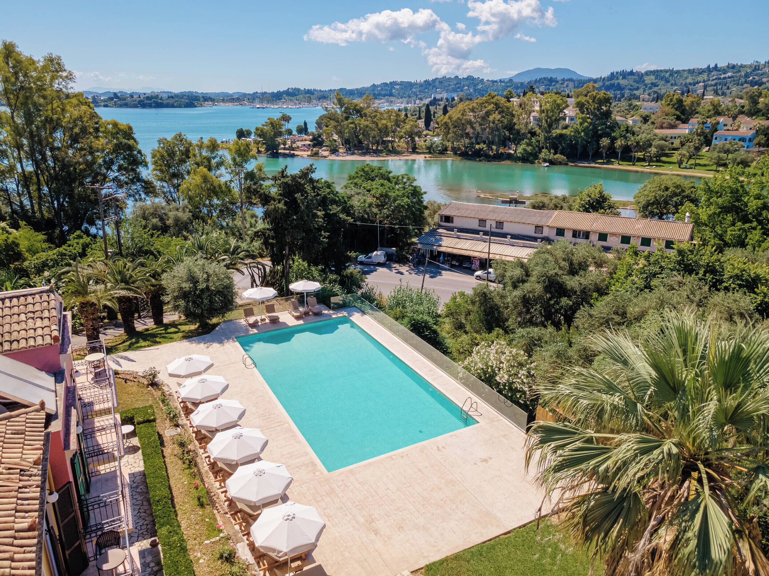 Ein Poolbereich mit Liegestühlen und Sonnenschirmen, umgeben von Grünflächen und Blick auf einen See sowie entfernte Hügel.