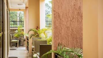A corridor with wicker furniture and potted plants, leading to a balcony with a view of greenery.