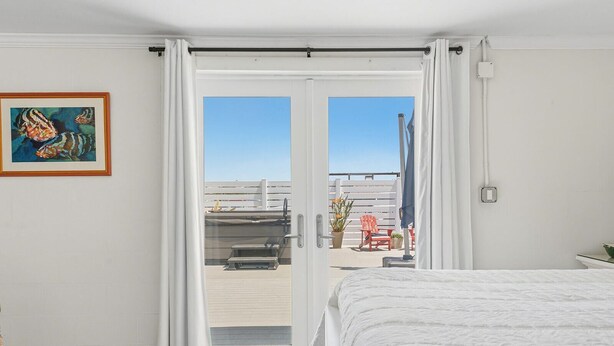 A hotel room with a bed, a door leading to a balcony, a framed painting, and a view of the balcony area.