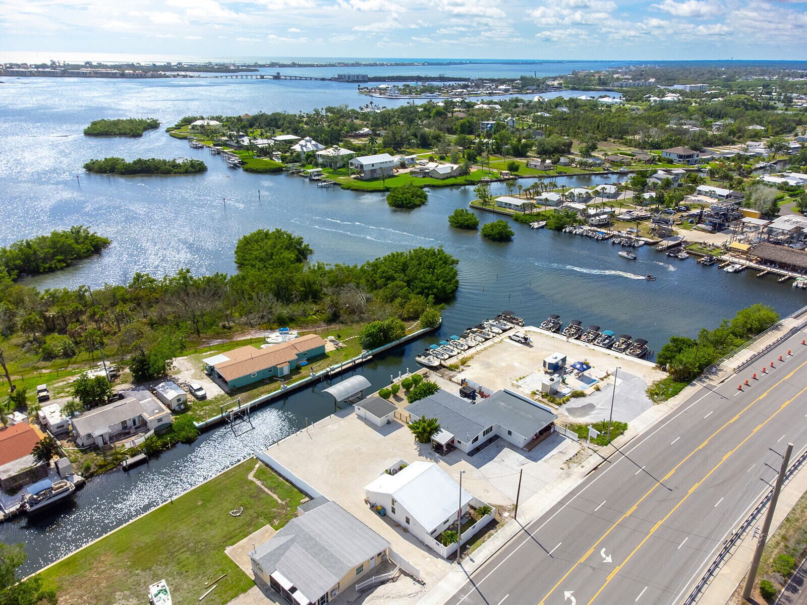 A marina with boats docked, a road adjacent to the water, and residential buildings.