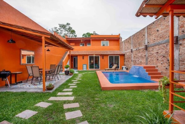 A backyard with a swimming pool, a patio with chairs and a table, and a brick wall.