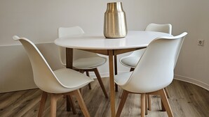Een eetgedeelte met een ronde tafel, vier witte stoelen en een metalen vaas.
